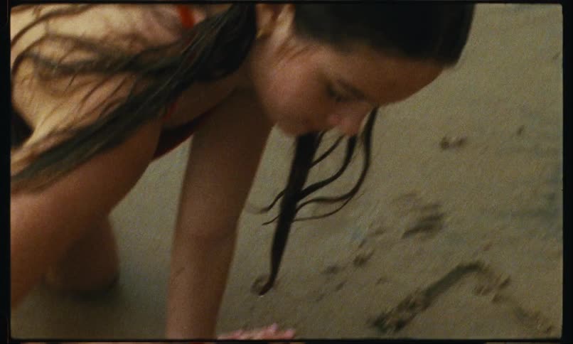 Girl wearing swimsuit writes letters in the beach sand with a stick