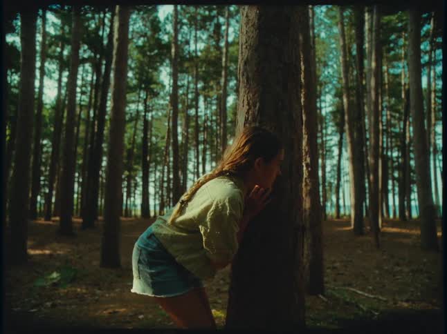 A young girl is playing in the woods peeking out from behind a tree