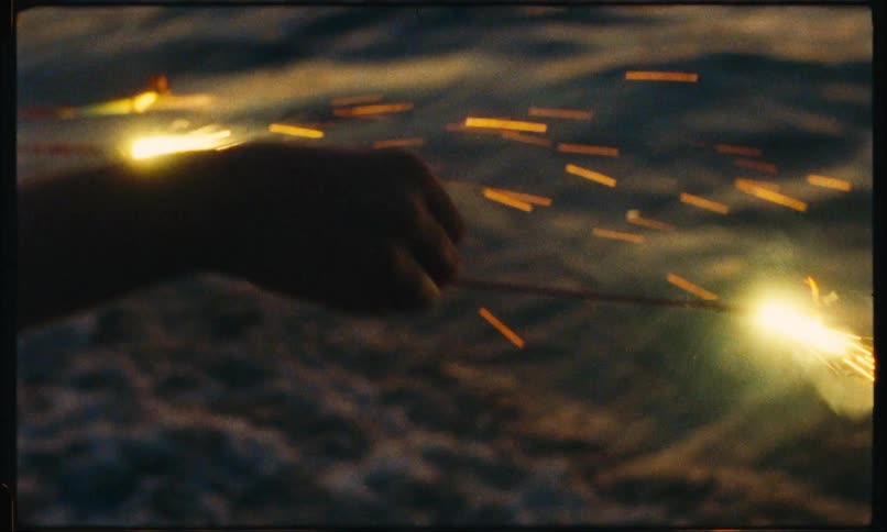 A person holding bright lights at the edge of the beach