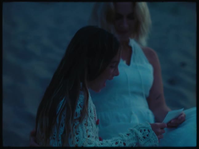 Mother and daughter sitting on beach after dusk smile while reading piece of paper