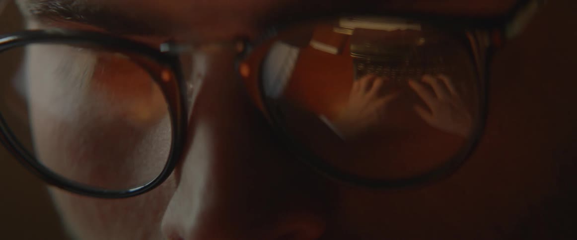 A man's hands as they work at a typewriter are reflected in his glasses