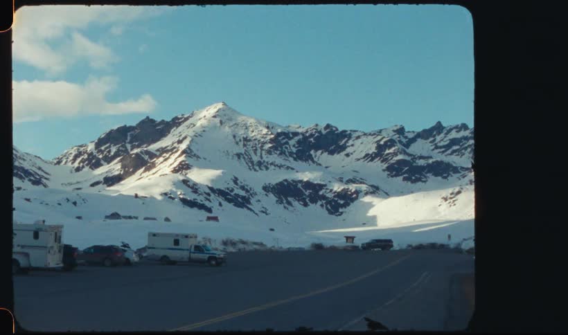 Some cars parked in an asphalt yard and behind a huge mountain covered in snow