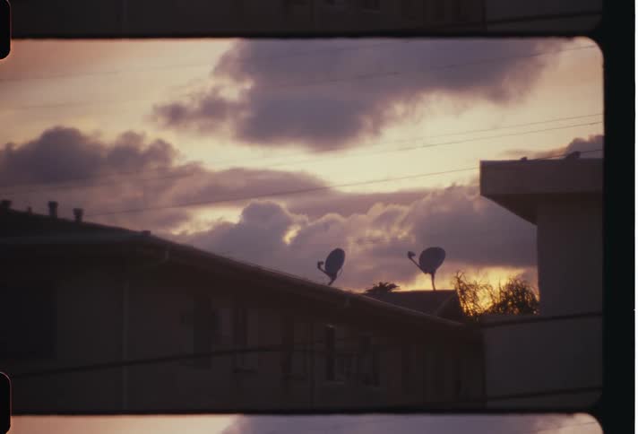 Clouds pass over houses on windy day as red tints the horizon