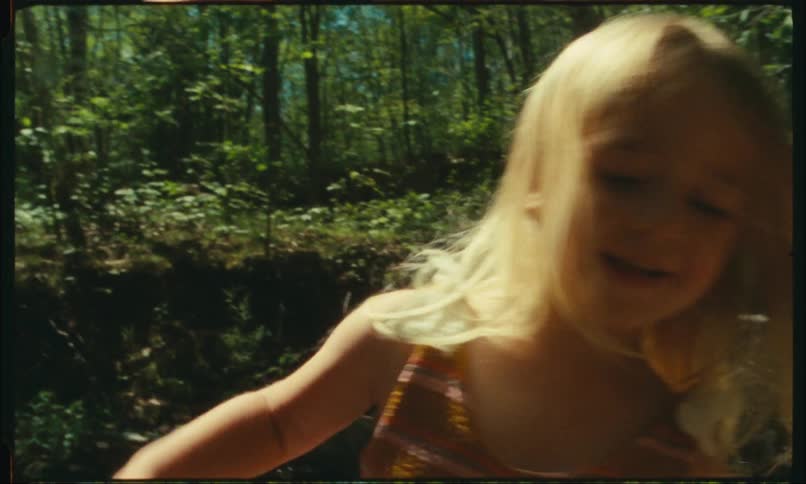 Closeup of a blonde little girl in the midst of a river in a forest in daylight
