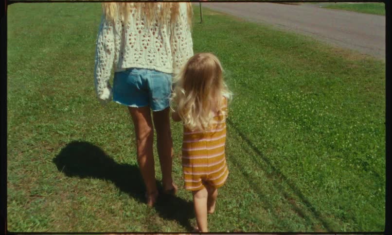 A girl walks on the grass near a neighborhood street with a little girl