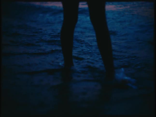 A silhouette of a person walking on the waves that are breaking at the seashore