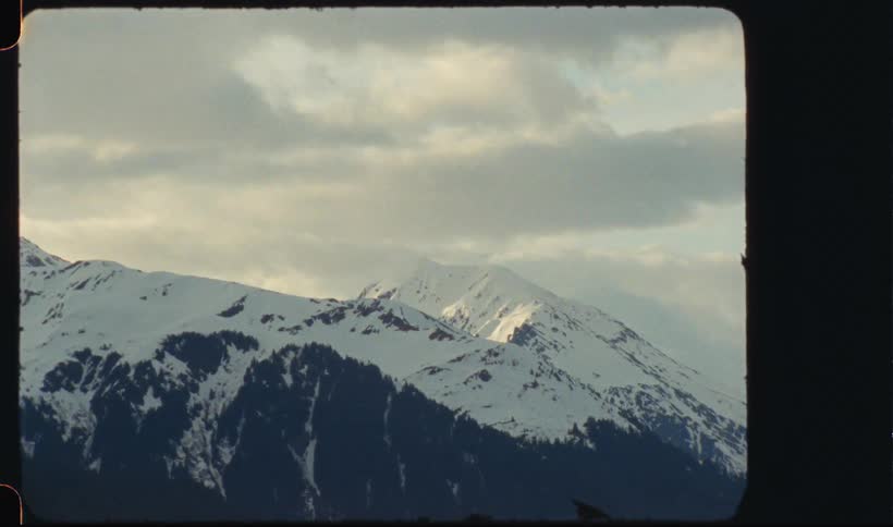 Snow covers mountains under a heavily clouded sky