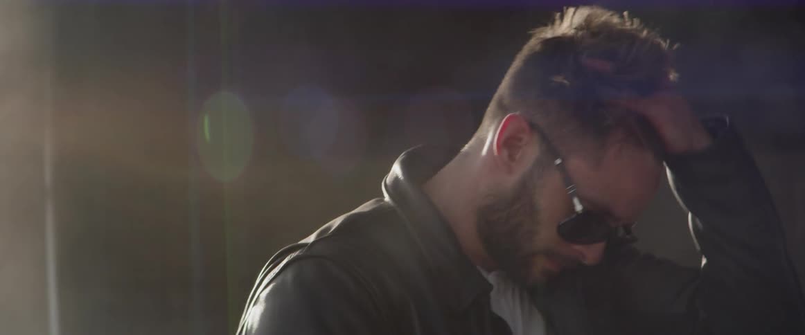 A man puts on a pair of sunglasses and brushes his hair with his hand