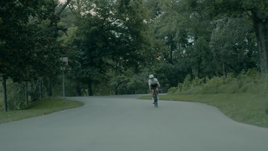 A man wearing a helmet is riding a bicycle on a road through a park