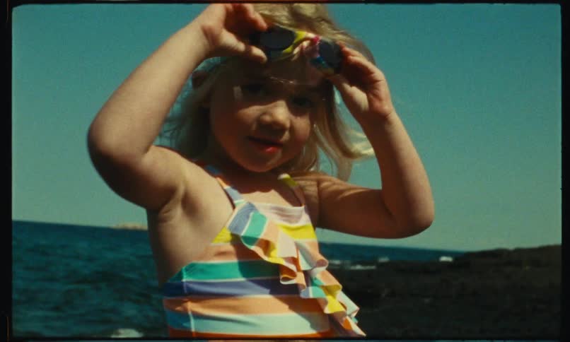 A small little girl holding her sunglasses on her head near the ocean