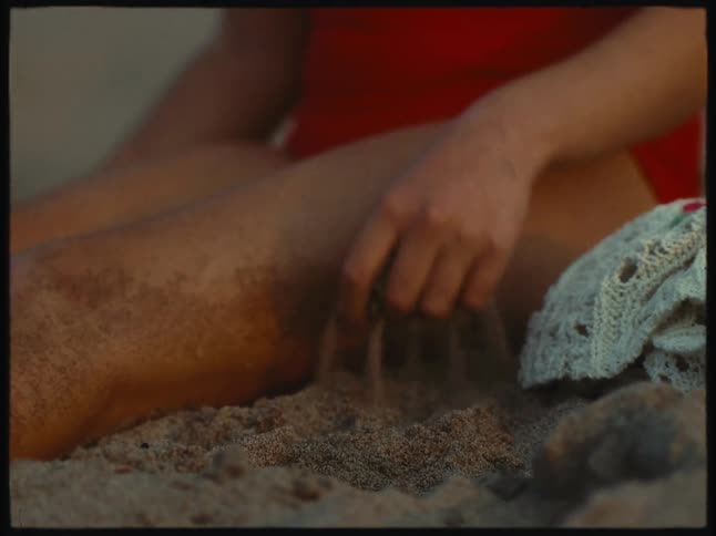 A child sitting on the sand is picking up the sand with his hand and throwing it on the ground again