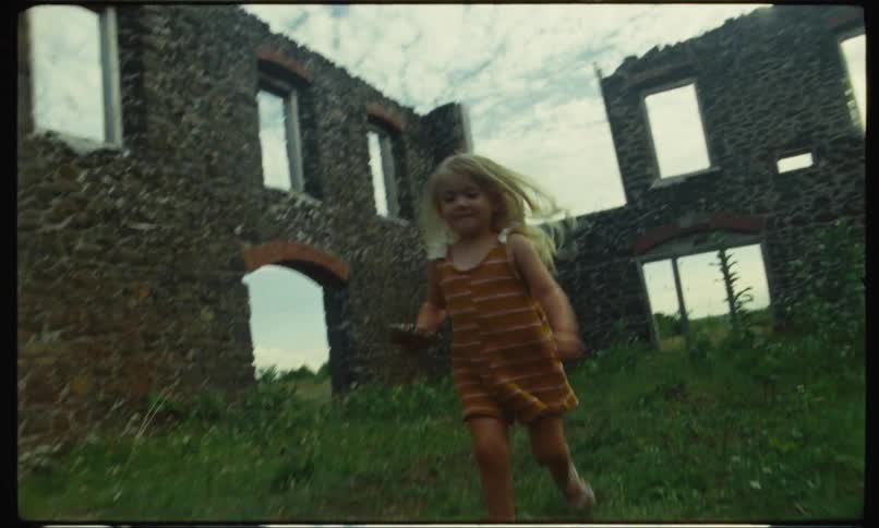 A young girl running happily in the grass among a castles ruins