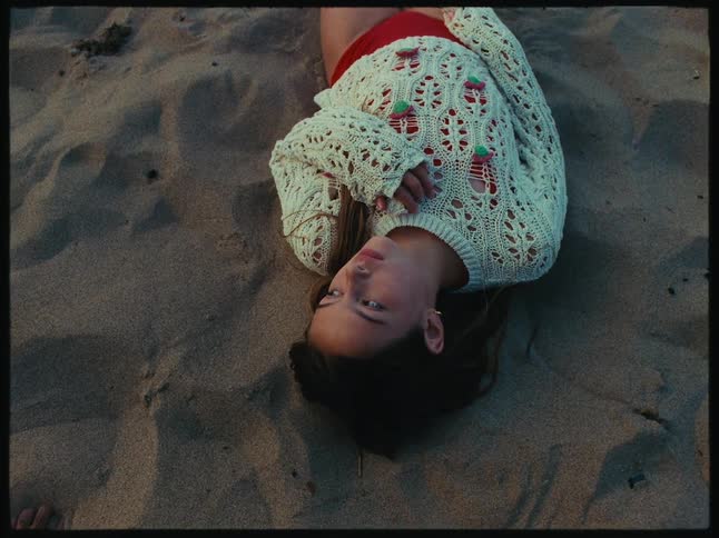 A woman wearing a shirt on her swim suit is lying down on the beach sand