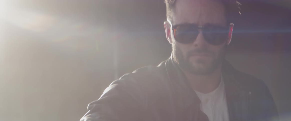 A man puts on his sunglasses before looking behind him