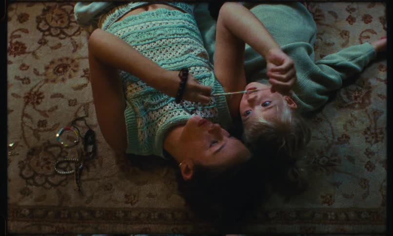 A toddler and a child are lying on the floor and the older one shows an object to the smaller one and she turns around