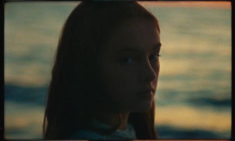 Closeup of a young teenagers face with the sea in the background and an orange sky