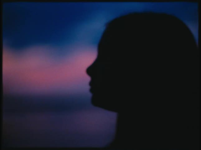 Woman silhouetted against red tinted horizon over the ocean turns