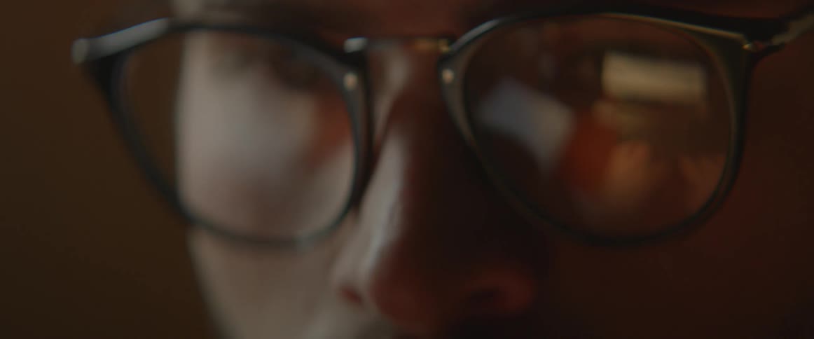 A reflection of a man typing is shown in the man's glasses