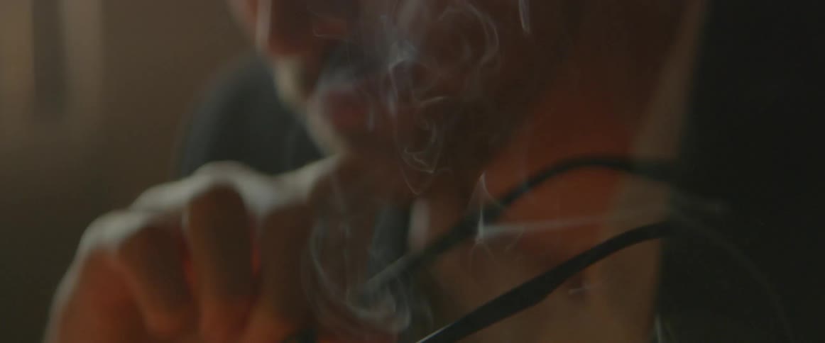 A man holds his glasses as smoke rises