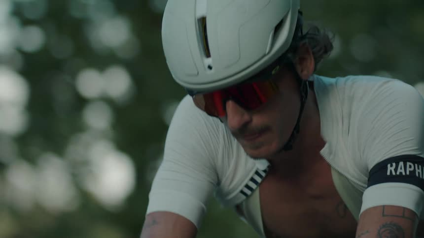 A man wearing sunglasses and a helmet is riding a bicycle on a road lined with trees