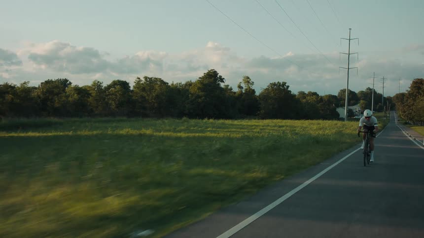A cyclist driving a bicycle on a rural road at morning