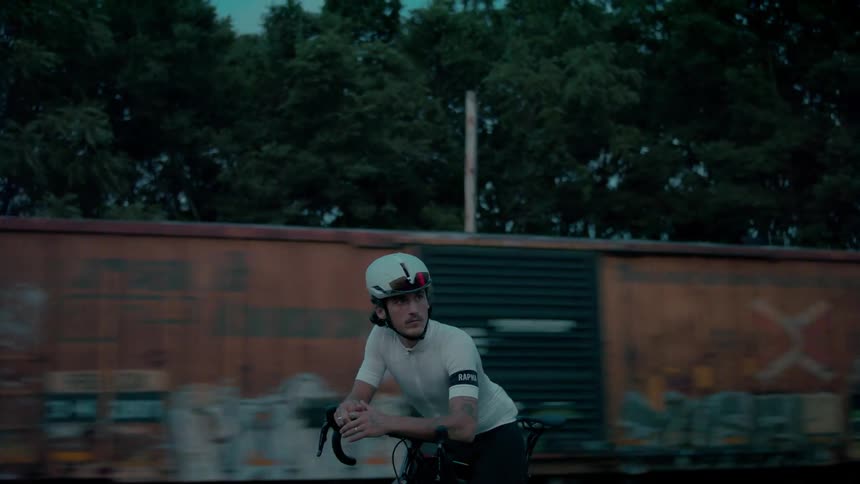 A man wearing a helmet is sitting on his bicycle as a train passes in the distance
