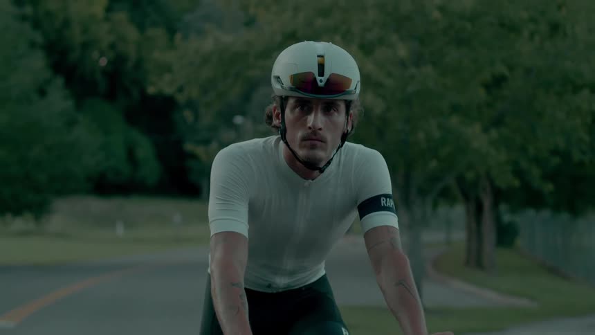 Man rides bicycle on highway past fenced park