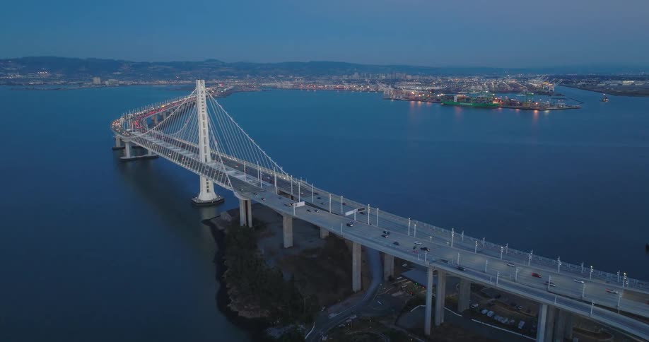 Aerial view of a suspension bridge connecting to a cityscape with lights in the distance