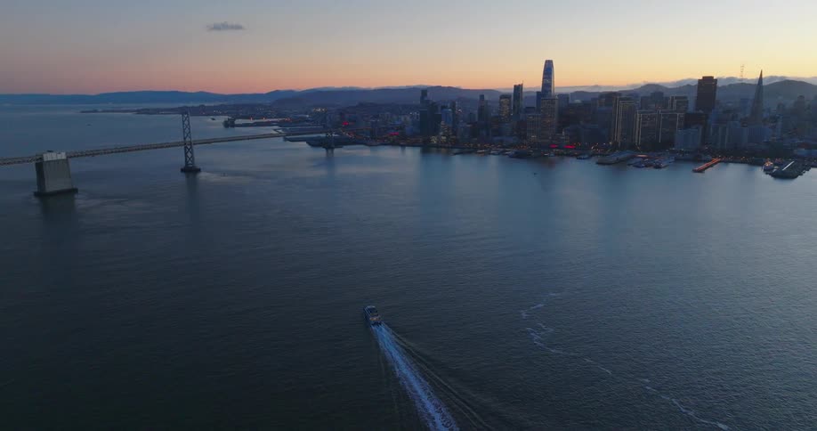 A boat driving on a river leading into a city at sun down