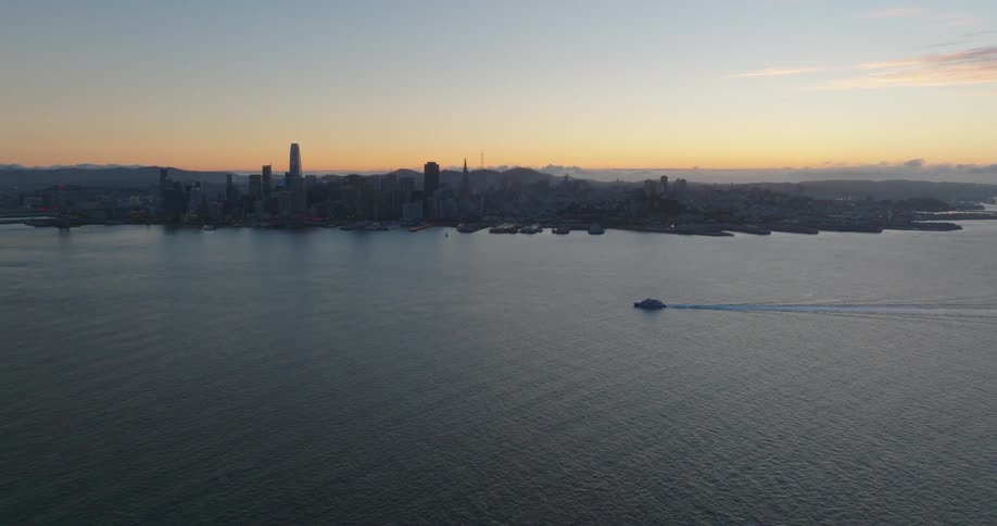 Aerial view of a ferry in front of the city skyline at sunset