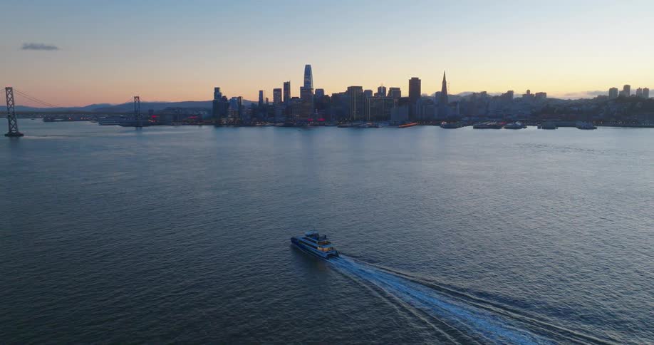 Aerial panorama of a boat sailing in the sea next to a metropolis with skyscrapers under an orange dawn sky