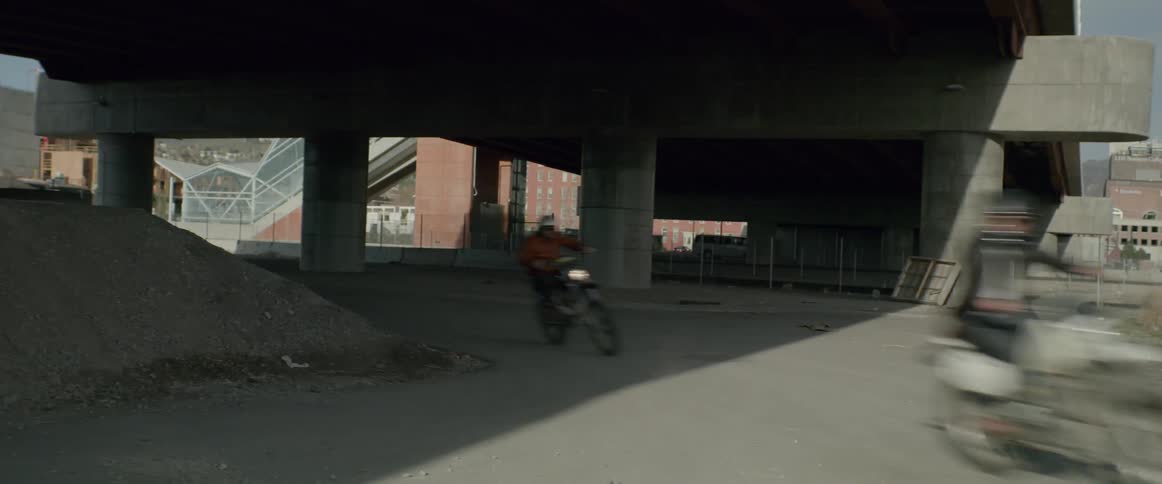 Motorcyclists speed under a bridge overpass