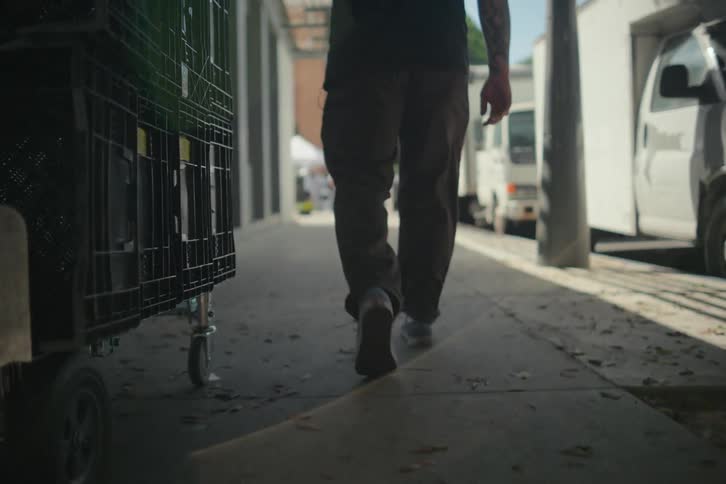 A man i dragging a roling bin with wheels on the side walk during the day