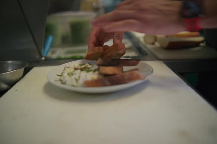 More than one person taking pieces of bread and placing them on a plate of food