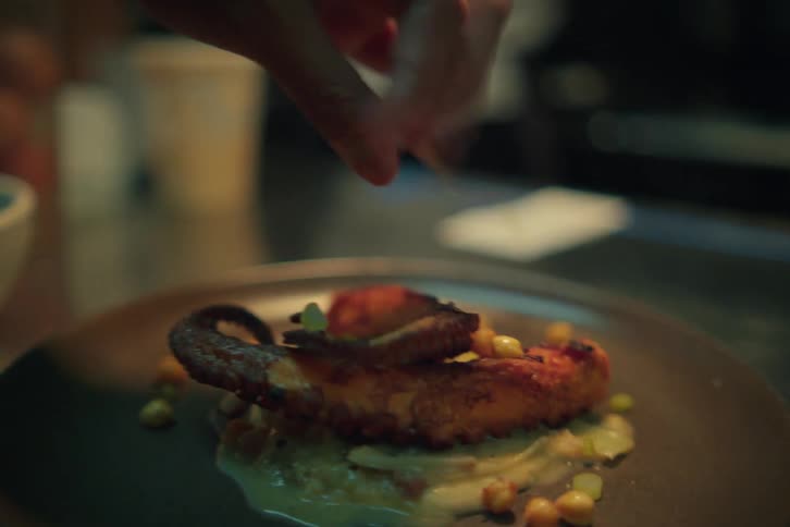 A chef serving an octopus dish in a restaurant kitchen