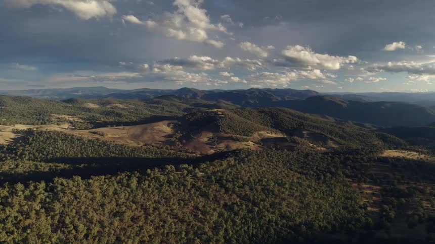 Aerial view of a road through countryside in a valley surrounded by hills with green vegetation with white clouds suspended in a sky at sunset