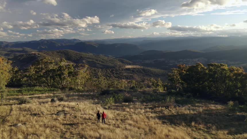 Aerial view of two hikers looking at the mountains from a grassy hill
