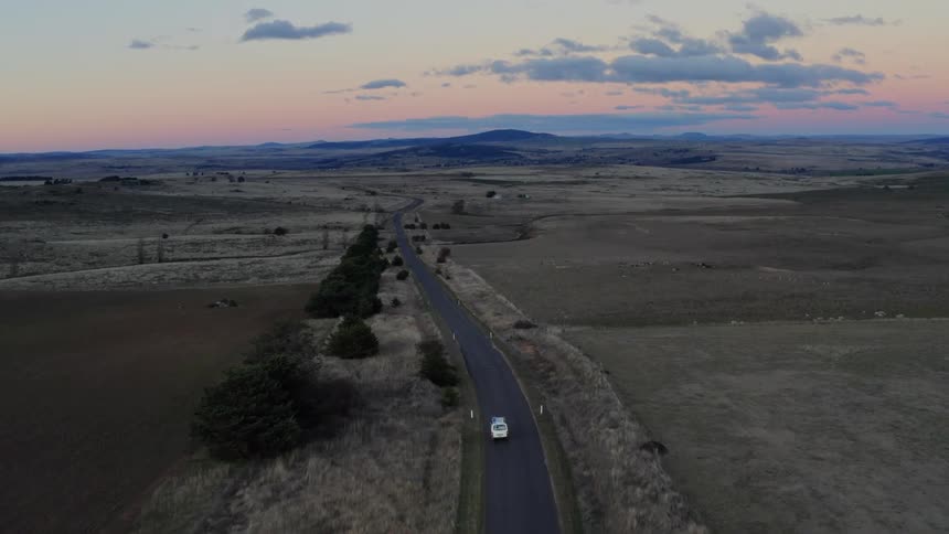 Aerial view of a car driving through the countryside at sunset
