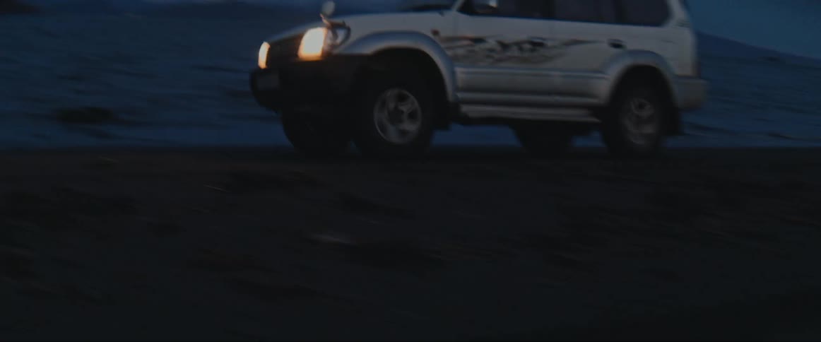 White car driving next to the ocean at evening