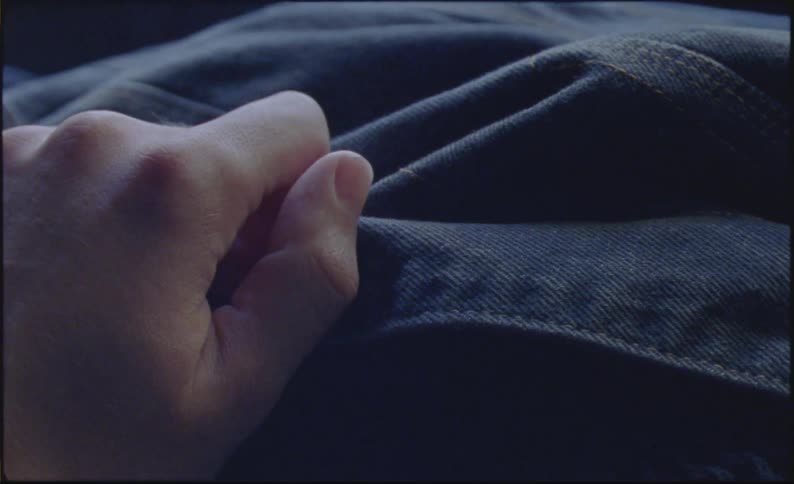 Close up of a hand tugging on a metal button on a jean jacket