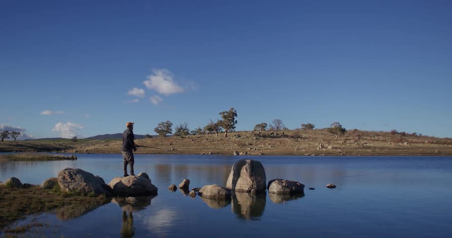A man standing on rocks in a lake fishing