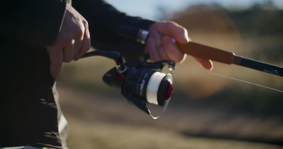 A closeup of a persons hands holding a fishing rod and reel in a sunny field