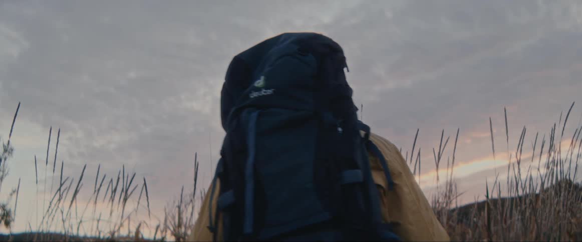 A hiker with a large backpack in a grassy field at dawn or dusk