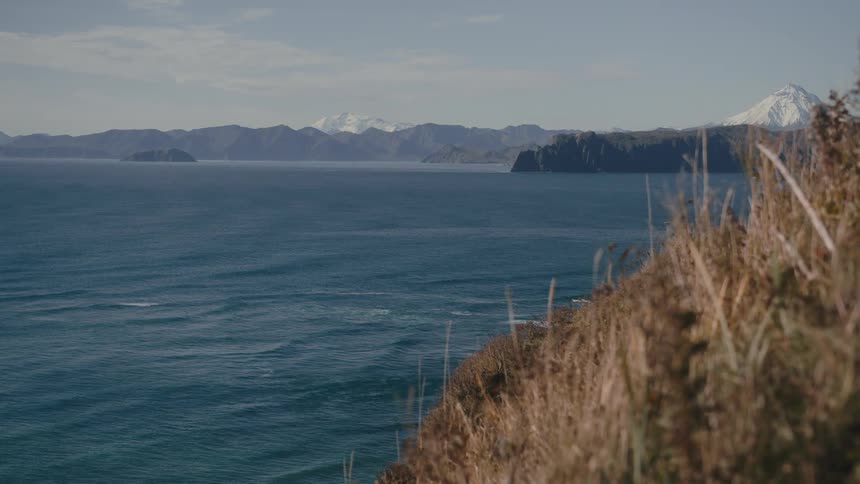 A nature scene with blue sea green grass and rocky mountains