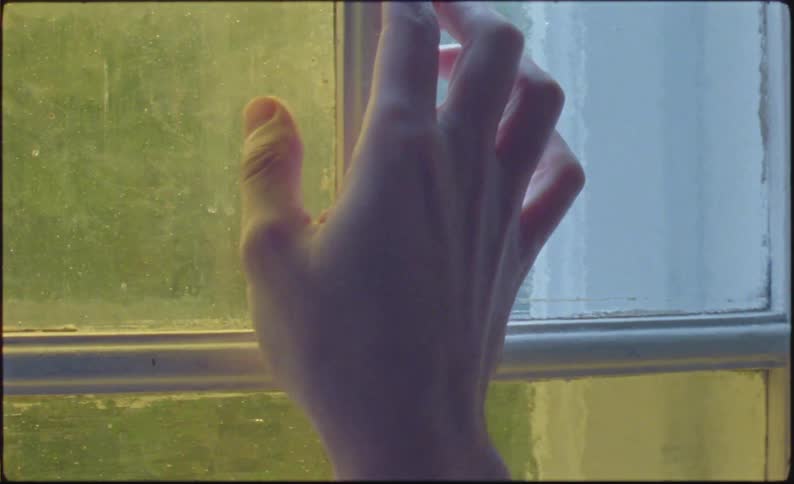 A hand reaching for a window with textured glass panes
