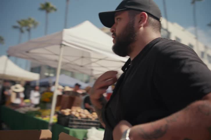 Man stacks boxes of produce near truck at outdoor market in plaza