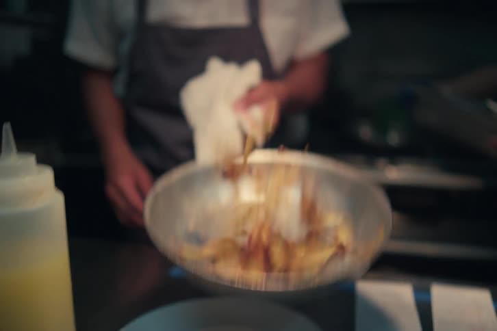 A cook flips food in a pan and serves it on a plate