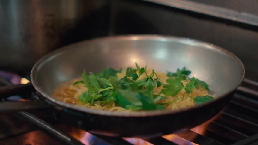 Fresh green herbs added to a pan of pasta in the kitchen