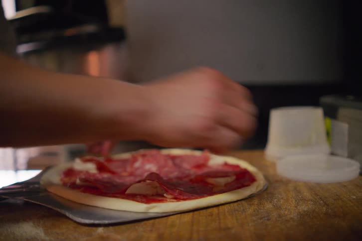 A man prepares a small pizza and places it into an oven to cook