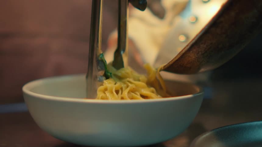 A closeup of noodles being served from a pot into a bowl